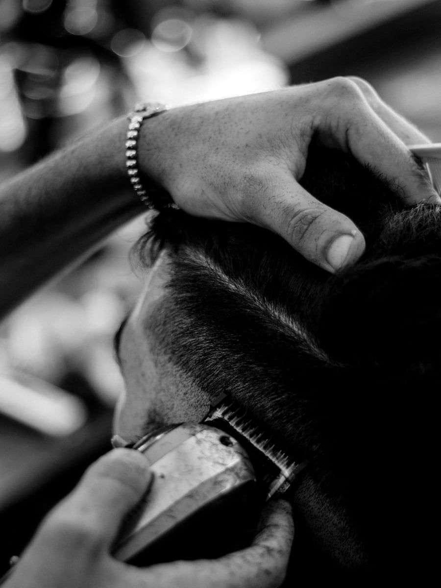 A barber steadying a client's head while running clippers up the side, close enough to see the guard against the skin.